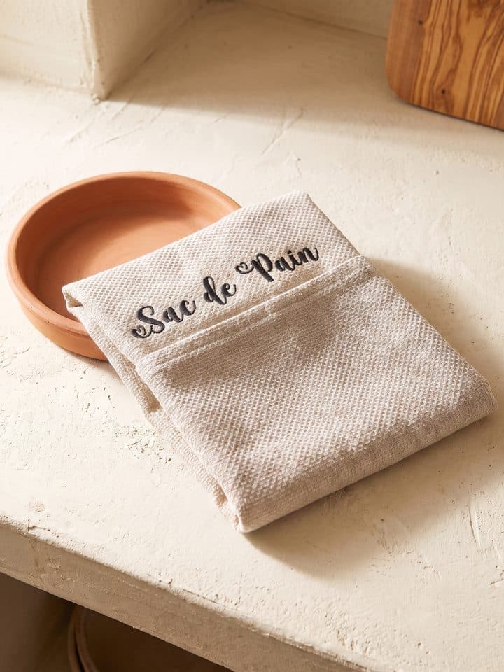 Sac de pain écru plié sur un plat en terre cuite
